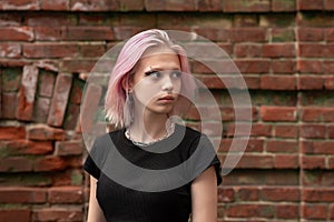 Portrait of a teenage girl with pink hair on a brick wall background