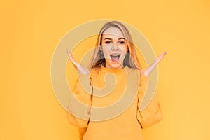 Portrait of a teenage girl with a shocking face, wearing orange clothes, standing on a yellow background and looking into the