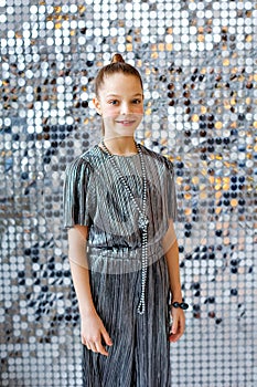 Portrait of a teenage girl in a silver jumpsuit on a background of silver sequins