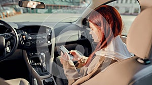 Portrait of teenage girl smiling at the screen while using her phone, sitting in the car. View from the back seat