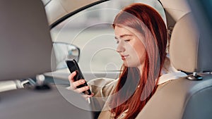 Portrait of teenage girl smiling at the screen while using her phone, sitting in the car. View from the back seat