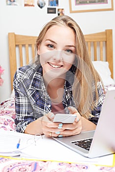 Portrait Of Teenage Girl Using Mobile Phone Whilst Doing Homework