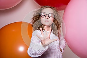 Portrait of a teenage schoolgirl showing five fingers on a background of large rubber balls.