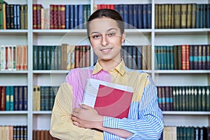 Portrait of teenage student with books in hands looking at camera in school library