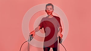 Portrait of teenaged disabled boy with cerebral palsy looking away, taking steps with his walker isolated over red light