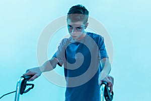 Portrait of teenaged disabled boy with cerebral palsy looking at camera, taking steps with his walker  over blue
