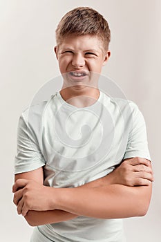 Portrait of teenaged disabled boy with Down syndrome grimacing at camera while posing with arms crossed isolated over