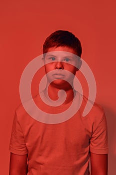 Portrait of teenaged disabled boy with Down syndrome looking scared at camera while posing isolated over red light