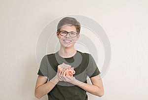 Portrait of teenager boy holding piggy bank and coin. Cute caucasian young teenager on white background. Saving Money concept.