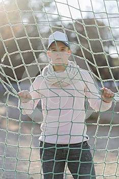 Portrait of teenager with cap behind a rope net in a park looking away