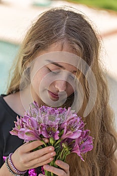 Portrait of a teenager girl with blonde hair smelling beautiful purple flowers