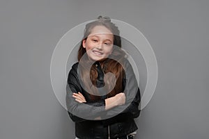 Portrait of a teenager girl with long hair in a black leather jacket on a gray background