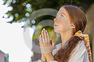 Portrait of teenager girl praying closed eyes to God asking for blessing help forgiveness outdoors