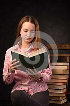 Portrait of a teenager girl reading book near the stack of books.