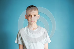 Portrait of a teenager in a gray t-shirt in the studio. Photo of an adorable young boy looking at camera on a blue background.