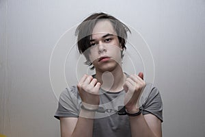 Portrait of a teenager in handcuffs on a gray background, medium plan. Juvenile delinquent, criminal liability of minors.