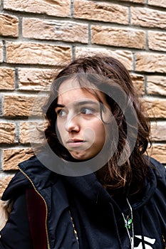 Portrait of teenager turkish girl in front of bricks wall. Black wearing teen looking aside