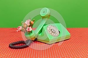 Portrait with telephone receiver and flowers inside on festive red table over green studio background. Creative