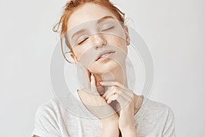 Portrait of tender girl with foxy hair and closed eyes smiling.