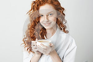 Portrait of tender redhead girl with freckles smiling holding cup looking at camera. White background.