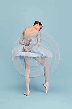Portrait of tender young ballerina dancing, performing isolated over blue studio background. Delightful performance