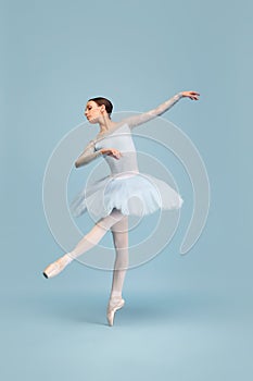 Portrait of tender young ballerina dancing, performing isolated over blue studio background. Graceful dance