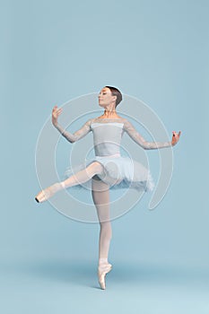 Portrait of tender young ballerina dancing, performing isolated over blue studio background. Graceful movements