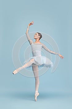 Portrait of tender young ballerina dancing, performing isolated over blue studio background. Graceful theatrical