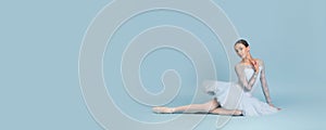 Portrait of tender young ballerina dancing, performing, sitting on floor isolated over blue studio background. Flyer