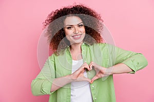 Portrait of thankful positive girl with wavy hairdo wear green shirt showing heart symbol on chest isolated on pink