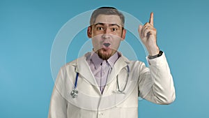 Portrait of thinking pondering doctor man in medical coat having idea moment pointing finger up on blue studio