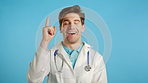 Portrait of thinking pondering doctor man in medical coat having idea moment pointing finger up on blue studio