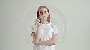 Portrait of thinking pretty young woman having idea, pointing with finger up, looking at camera, standing on white