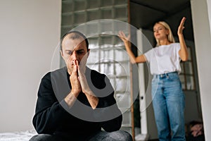 Portrait of thinking stressed man sitting on bed sadness looking away ignoring angry girlfriend arguing blaming upset