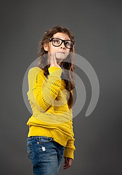 Portrait of thinking style schoolgirl in eyeglasses looking up on grey studio background in fashion clothing. Back to school