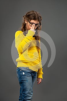 Portrait of thinking tired unhappy schoolgirl in eyeglasses looking up on grey studio background in fashion clothing