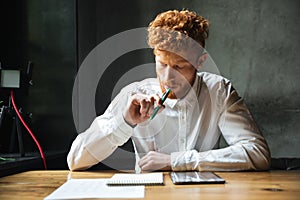 Portrait of thinking young readhead man in white shirt, sitting