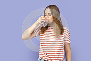 Thirsty attractive beautiful young adult blond woman drinking water from glass, healthy eating.