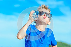 Portrait of a thirsty handsome boy in sunglasses drinking water