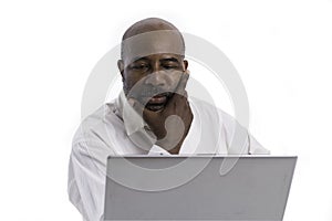 Portrait of thoughful and pensive African American software expert sitting front of a laptop computer.   Contemplating man working