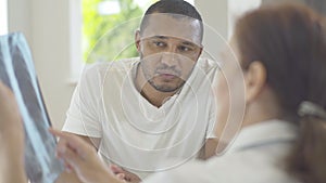 Portrait of thoughtful African American man listening to blurred Caucasian woman explaining disease complications on