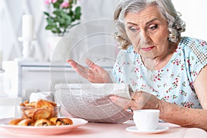 Portrait of thoughtful aged woman reading newspaper