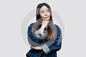 Portrait of thoughtful beautiful brunette asian young woman in casual blue denim jacket with makeup standing, confused looking