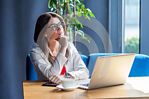 Portrait of thoughtful beautiful stylish brunette young woman in glasses sitting, looking away and planning new idea or thinking
