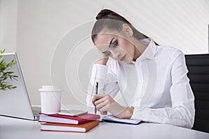 Portrait of a thoughtful brown haired businesswoman in a white blouse sitting at her table in an office.