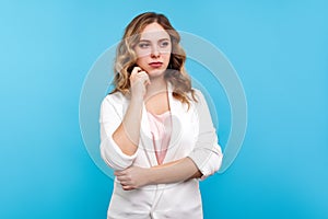 Portrait of thoughtful business woman with wavy hair in white jacket looking away, musing, pondering with confused puzzled face,