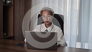 Portrait of thoughtful concerned middle-aged adult 50s woman working on laptop computer in office looking to screen