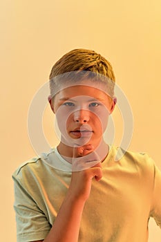 Portrait of thoughtful disabled boy with Down syndrome looking at camera, holding hand on chin while posing isolated