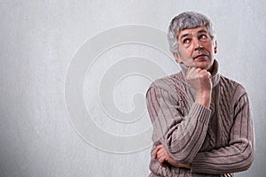 A portrait of thoughtful dreamy senior man standing over white background with copy space for your advertisement. Mature man deep