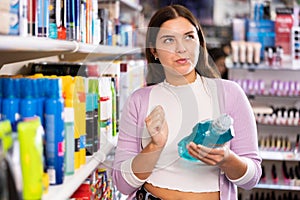 Portrait of thoughtful female customer choosing suitable hair care products at cosmetics store